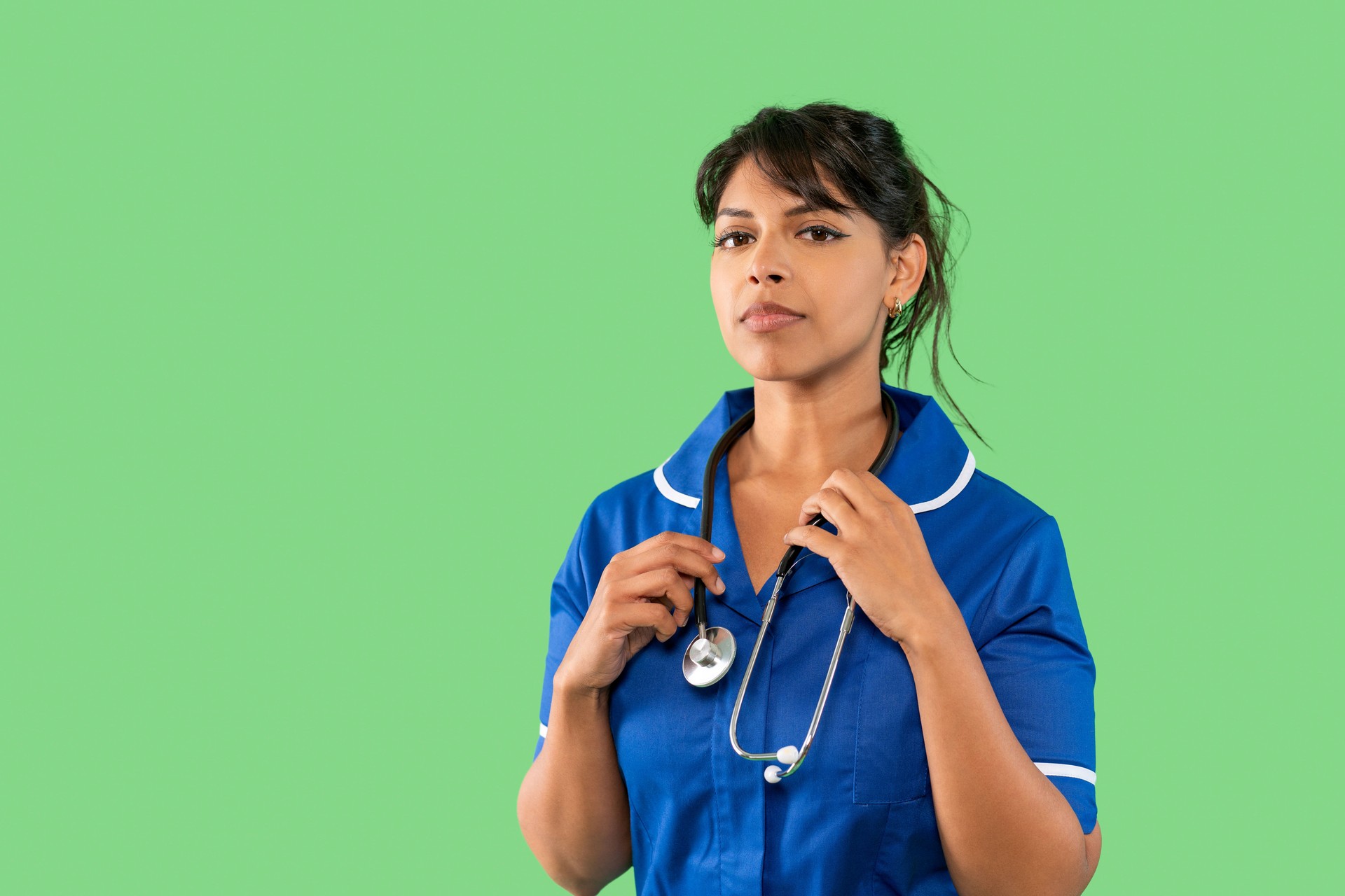 Nurse wearing scrubs and stethoscope against a green background in a healthcare setting while preparing for patient care